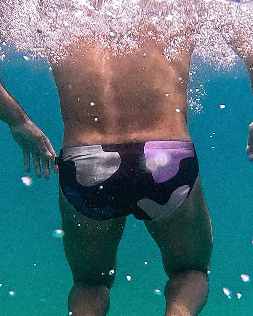 Person swimming underwater wearing swim trunks with a visible brand logo.