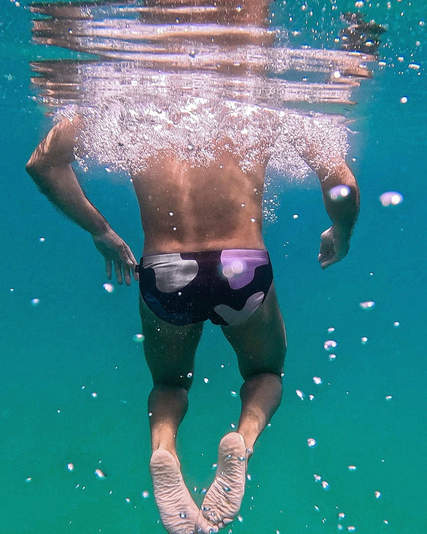 Person swimming underwater wearing swim trunks with a visible brand logo.