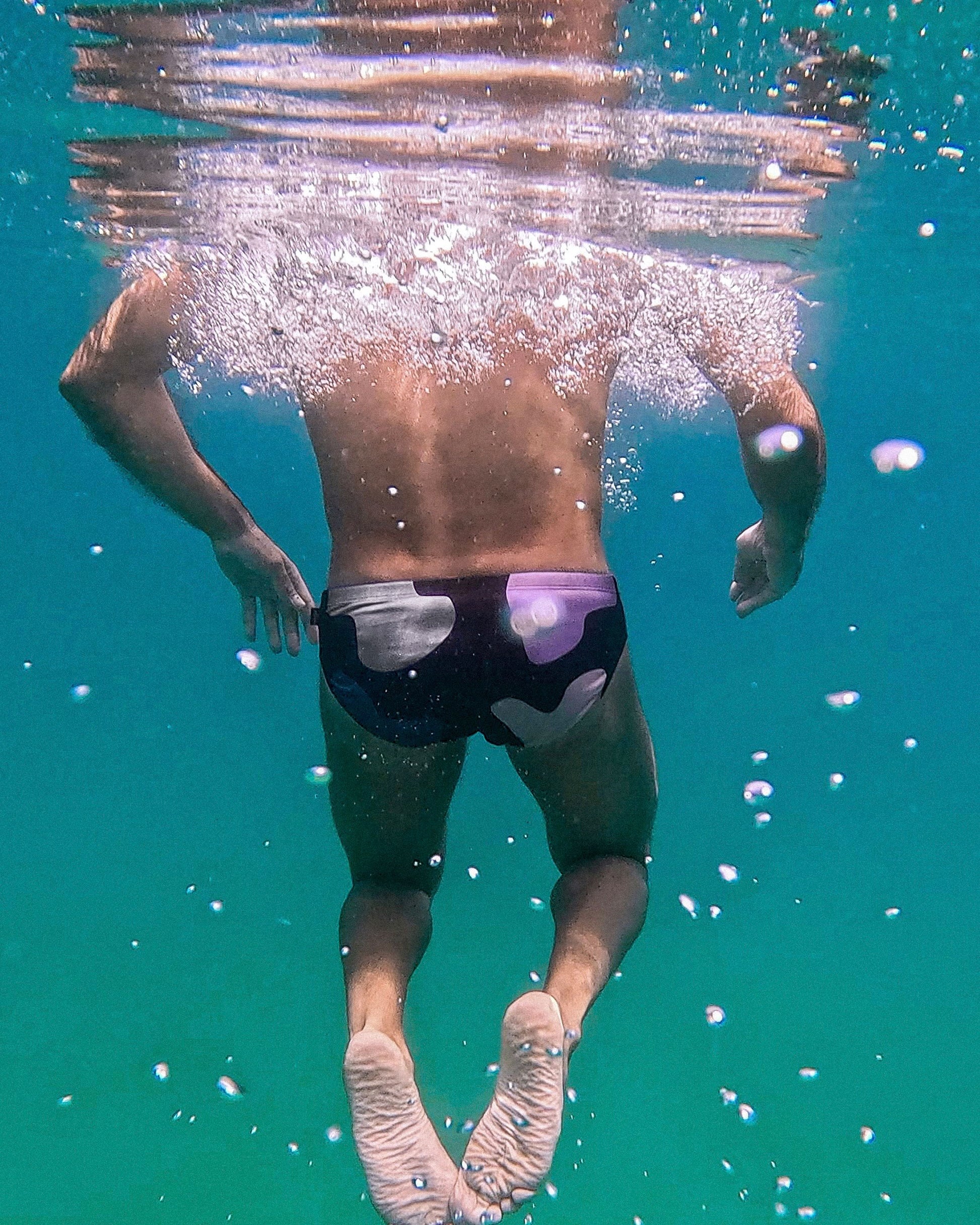 Person swimming underwater wearing swim trunks with a visible brand logo.