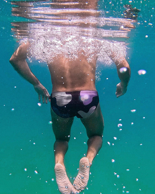 Person swimming underwater wearing swim trunks with a visible brand logo.